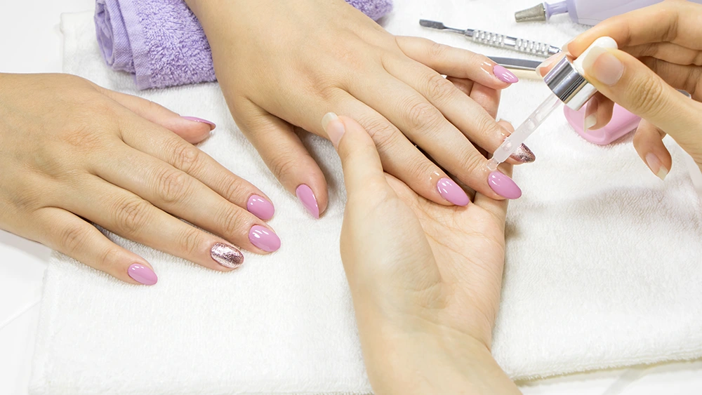 The manicurist applies oil to the cuticle