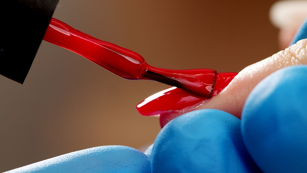 Manicurist paints nails with red gel polish